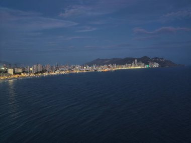 Gece sahili aydınlık, uzak kıyı şeridi şehir siluetiyle deniz feneri ışıkları