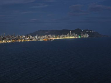 Geceleri kıyı şeridi boyunca ışıklar, akşam saatlerinde gemileri ve aydınlık yapıları olan sessiz körfez.