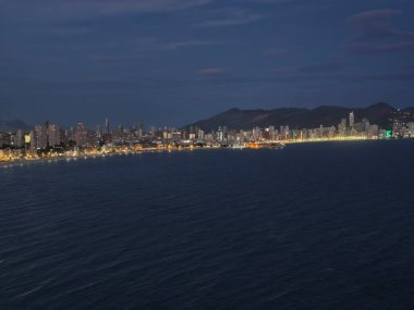 Sakin sahil ve dağ manzarası parıldayan şehir yansımaları ve yumuşak deniz ile gece gökyüzü altında