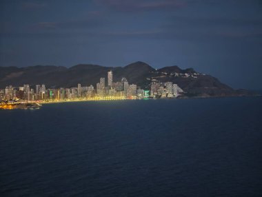 Sakin sahil şehri ışıkları alacakaranlıkta, sakin okyanus şehir ışıklarını yansıtan dağ gölgeleri altında