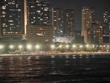 Sakin gökyüzü altında aydınlık bir sahil yürüyüşü. Parlak ışıklarla ve uzak mesafelerle sakin bir sahil akşamı.
