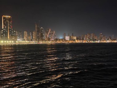 Dalgalanan dalgalanan dalgalar ve parlak gölgelerle deniz silueti atmosferik kentsel manzarayı çerçeveliyor