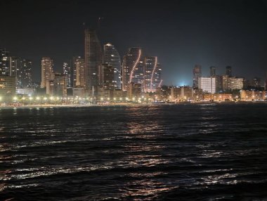 Gökdelenler ve turnalar gelişmeyi simgeler, gece şehir manzarası genişlemeyi ve ekonomiyi yansıtır