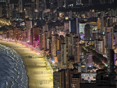 Canlı bir sahil akşamı, ışıl ışıl yürüme yolları ve ışıl ışıl kıyı şeridi olan canlı bir gece plajı.