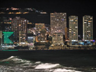 Canlı kentsel ufuk çizgisi sakin suları renkli yansımalar ve canlı atmosferle aydınlatıyor.