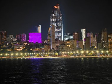 Canlı kentsel ufuk çizgisi sakin suları renkli yansımalar ve canlı atmosferle aydınlatıyor.