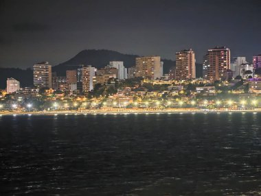 Canlı kentsel ufuk çizgisi sakin suları renkli yansımalar ve canlı atmosferle aydınlatıyor.