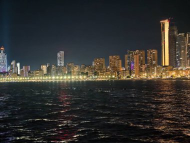 Canlı kentsel ufuk çizgisi sakin suları renkli yansımalar ve canlı atmosferle aydınlatıyor.