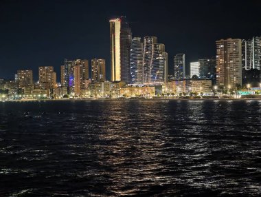 Canlı kentsel ufuk çizgisi sakin suları renkli yansımalar ve canlı atmosferle aydınlatıyor.