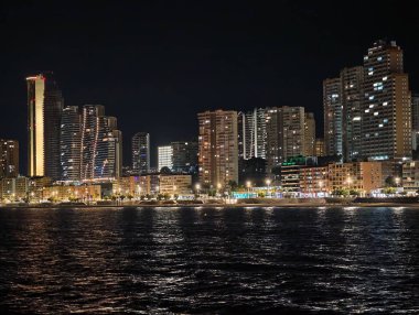 Canlı kentsel ufuk çizgisi sakin suları renkli yansımalar ve canlı atmosferle aydınlatıyor.