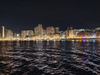 Canlı kentsel ufuk çizgisi sakin suları renkli yansımalar ve canlı atmosferle aydınlatıyor.