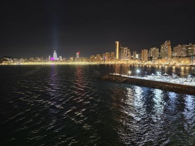 Canlı kentsel ufuk çizgisi sakin suları renkli yansımalar ve canlı atmosferle aydınlatıyor.