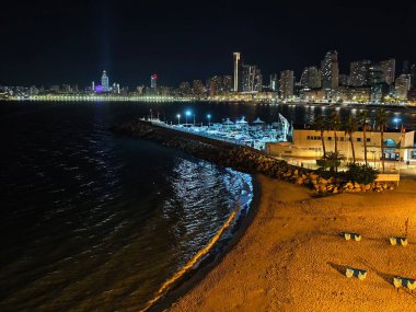 Canlı kentsel ufuk çizgisi sakin suları renkli yansımalar ve canlı atmosferle aydınlatıyor.