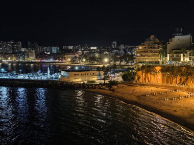 Sakin kıyı şeridi sıcak lambalarla aydınlanıyor, aydınlık körfez alanı, nazik dalgalar ve şehirlerle aydınlanıyor.