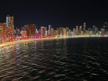 Gece şehir manzarası parıldayan yansımalarla, panoramik deniz manzarası ışıl ışıl parlıyor.