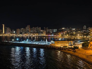 Sakin rıhtım yolu, sakin liman ve parlayan sokak ışıklarının olduğu huzurlu gece manzarası.