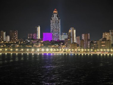 Gece silueti sergilendi, parlayan kuleler ve renkli cephelerle uzak okyanus manzarası