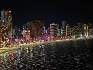 Canlı kıyı gecesi, enerjik rıhtım manzarası canlı ışıklar ve yüksek gökdelenlerle aydınlatılıyor.