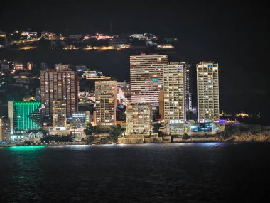 Işıklı şehir manzarası, parlak binaların ve yansıtıcı suların yer aldığı şehir sahnesi
