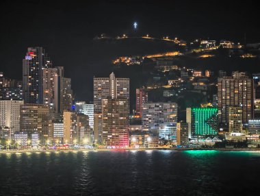 Kıyı boyunca parlak şehir ışıkları gece fotoğrafçılığı ve turizm için canlı bir atmosfer yaratır.