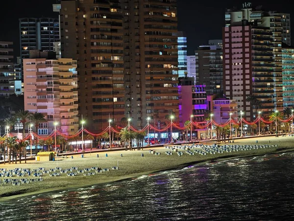 Parlak gece kıyısı, renkli kumsallar, hareketli satıcılar ve parıldayan ıslak kumlar.