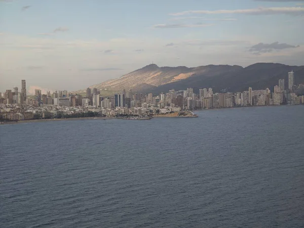 Huzurlu okyanus ve şehir manzarası, modern binalar ve günbatımının yer aldığı sakin kıyı şeridi