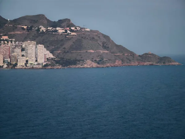 Sahil manzarası, huzur dolu körfeze bakan güzel kayalık binalar ve yelkenli gemiler.