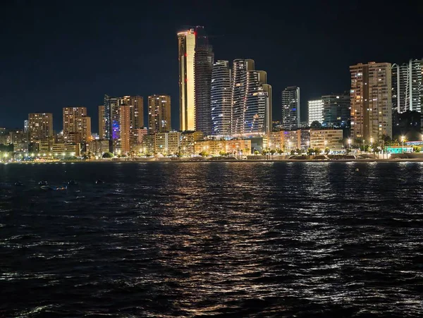 Canlı kentsel ufuk çizgisi sakin suları renkli yansımalar ve canlı atmosferle aydınlatıyor.