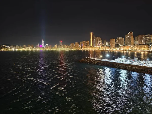 Canlı kentsel ufuk çizgisi sakin suları renkli yansımalar ve canlı atmosferle aydınlatıyor.