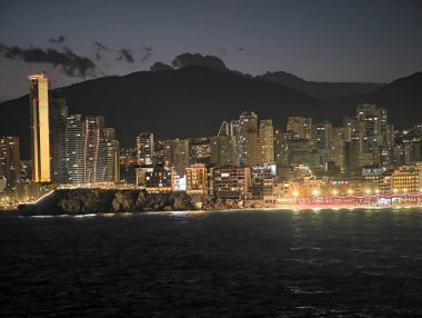 Parlak kuleler ve tatil ışıklarıyla aydınlatılan sakin kıyıların üzerinde canlı bir gece silueti.