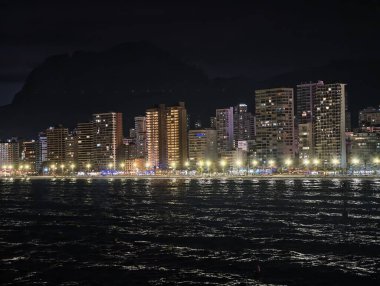 Huzurlu bir gece panoraması Parlayan sokaklar ve sessiz sahil boyunca yükselen binalar