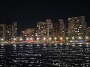 Akşam şehir manzarası, sakin deniz kenarı şehir silueti Lanternlit gezinti alanı altında parlıyor