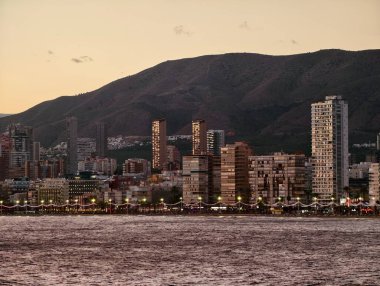 Sahil boyunca sakin su önü ve dağ manzaralı apartmanların akşam manzarası