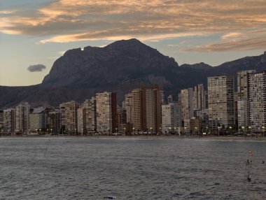 Akşam parlayan uzun gökdelenler okyanus kenarında uzak dağlar ve dramatik bulutlar