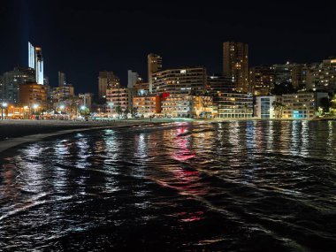 Parlak neon hatları dalgalı suların üzerinde parıldıyor. Gece gökyüzünün altında renkli şehir ışıklarını yansıtıyor.