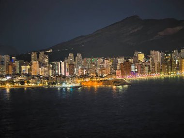 Şehir ışıkları suyu yansıtıyor, gece şehir manzarası ve dağ manzarası çok güzel yansıyor.