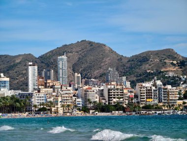 Arkaplanda yükselen dağlarla ve kumlu kıyılara çarpan okyanuslarla dolu canlı bir sahil kasabası.