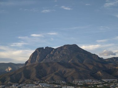 Kasaba manzaralı güneşli tepe, parlak dağ manzaralı mavi gökyüzünün altında tuhaf bir yerleşim yeri gözlemliyor.