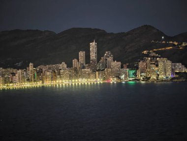 Gece vakti şehir panorama binaları sergiliyor ve sakin göle yansıyor.