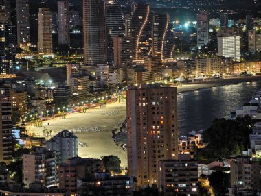 Gece kıyısı şehir manzarası, ışıl ışıl binaları ve canlı yürüyüş yolları olan canlı gece deniz önü.