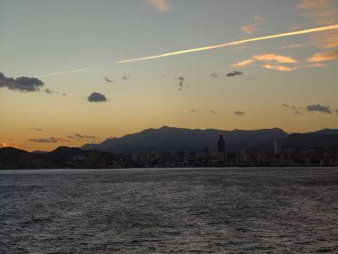 Huzurlu sular üzerinde sakin gökyüzü, sessiz pembe ve mavi gölgeler sakin bir kıyı arkaplanı oluşturur.