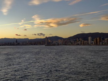 Sakin okyanus üzerinde günbatımı gökyüzü, sakin kıyı sularına bitişik metropolitan manzarası