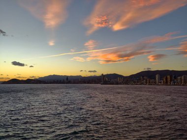 Gün batımı şehir manzarası, dağ manzaralı alacakaranlık ufku, sakin suya karşı akşam silüeti