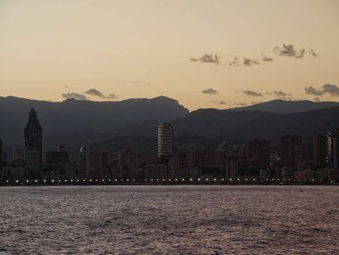Akşam liman sahnesi, gece gündüz dingin, sakin deniz manzaralı, parlayan ışıklar ve huzur dolu bir şehir.