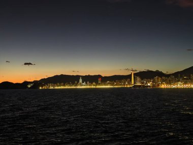 Manzaralı bir akşam sahili manzarası, gün batımında gezinti güvertesi boyunca uzak mesafeden yansımalar.