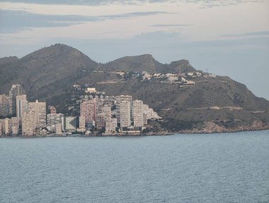 Ele geçirilen deniz kenarı manzarası sakin sular boyunca yoğun şehir binalarını aydınlatıyor.
