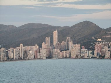 Kibar şafak, sahil kulelerini aydınlatıyor, sakin sabah, canlı şehir kıyılarında tepelerle parıldıyor.