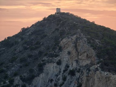 Kıyı mirası sahnesi, gün batımı yıpranmış taşları aydınlatıyor, tarihi kıyı şeridini sıcak kehribar ışığı kaplıyor.