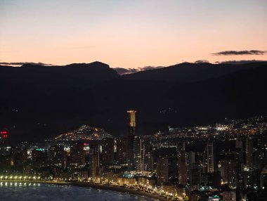 Akşam şehir ışıkları, sakin şehir manzarası alacakaranlıkta yumuşak tonlarla ve uzak dağlarla