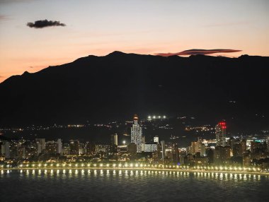 Parlak rıhtımlı kentsel alacakaranlık, sakin gece deniz manzarası canlı şehir siluetini yansıtıyor